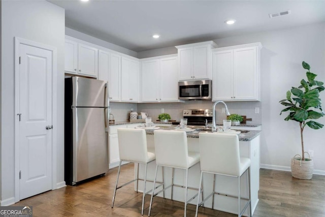 kitchen featuring appliances with stainless steel finishes, visible vents, wood finished floors, and an island with sink