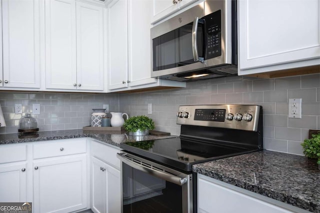 kitchen featuring stainless steel appliances, white cabinetry, decorative backsplash, and dark stone countertops