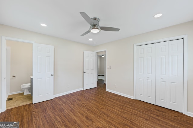 unfurnished bedroom featuring baseboards, ensuite bath, dark wood finished floors, and a closet