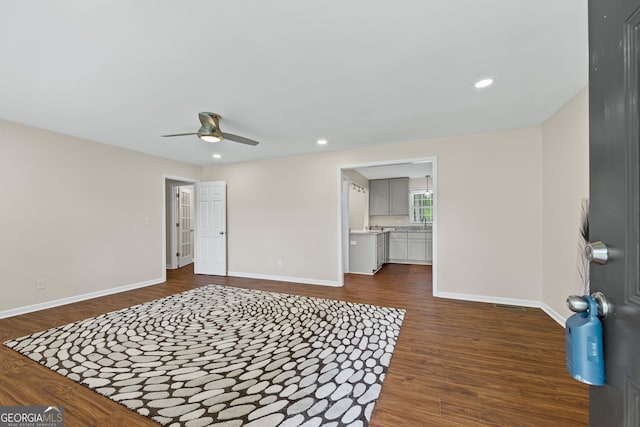 interior space with a ceiling fan, baseboards, and dark wood-type flooring