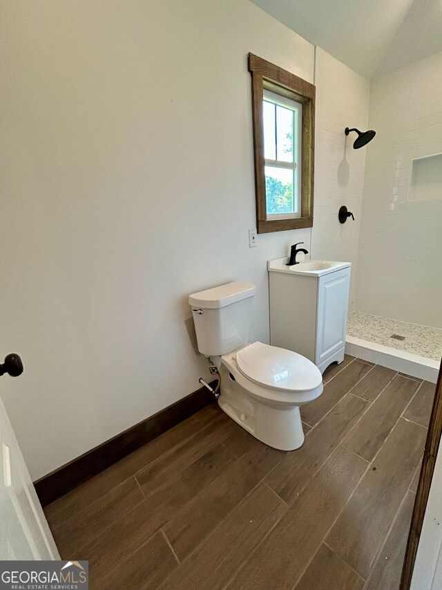 full bath featuring toilet, lofted ceiling, wood finished floors, vanity, and a tile shower
