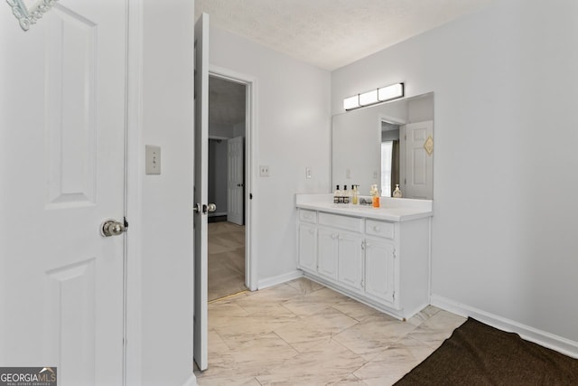 bathroom featuring a textured ceiling, baseboards, marble finish floor, and vanity