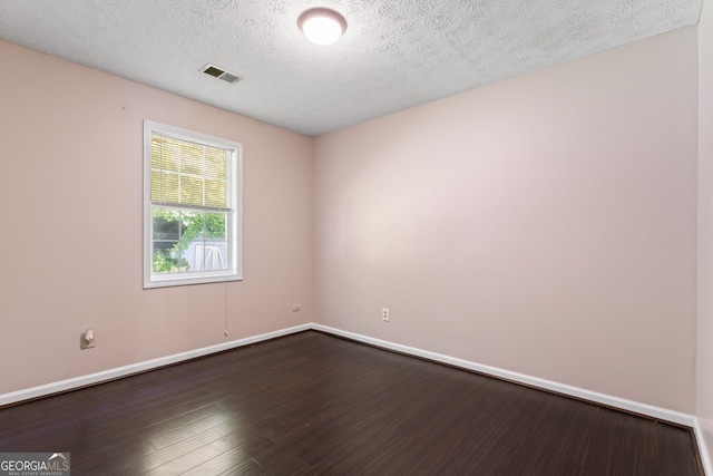 spare room featuring dark wood-style flooring, a textured ceiling, baseboards, and visible vents