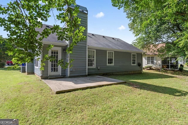 rear view of house featuring a lawn, a patio area, roof with shingles, and a chimney