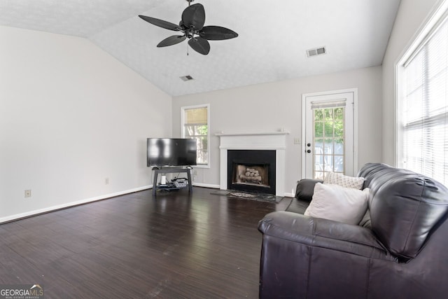 living room featuring a ceiling fan, a fireplace with flush hearth, dark wood finished floors, visible vents, and vaulted ceiling