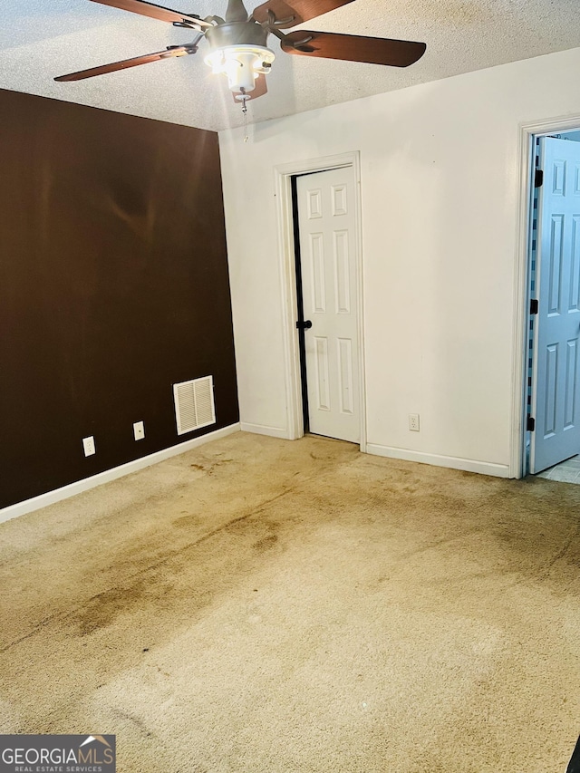 empty room featuring a textured ceiling, carpet, baseboards, ceiling fan, and visible vents