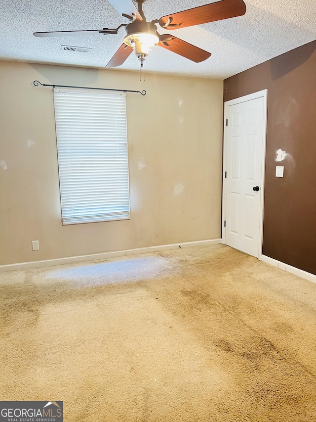 unfurnished room featuring ceiling fan, a textured ceiling, carpet floors, and visible vents