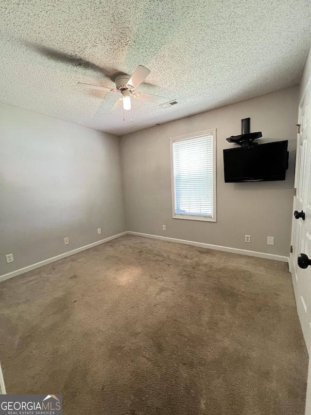 carpeted spare room featuring a textured ceiling, visible vents, baseboards, and a ceiling fan