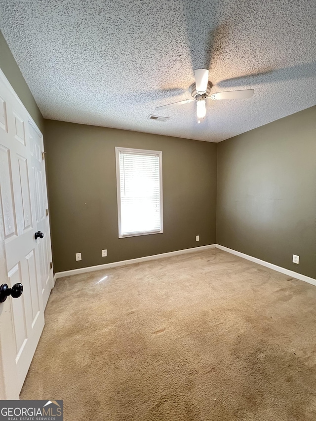spare room with carpet, a ceiling fan, a textured ceiling, visible vents, and baseboards