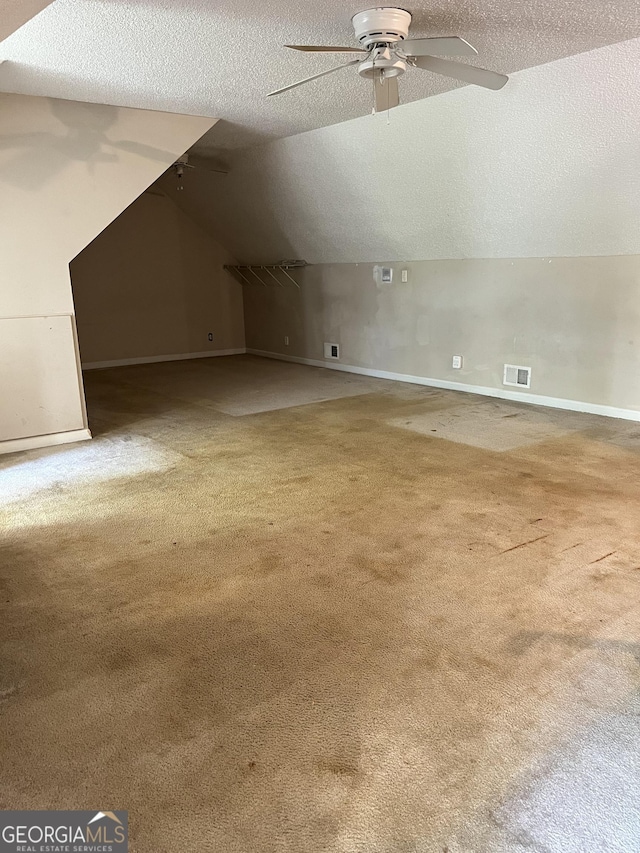 additional living space with vaulted ceiling, a textured ceiling, carpet floors, and visible vents