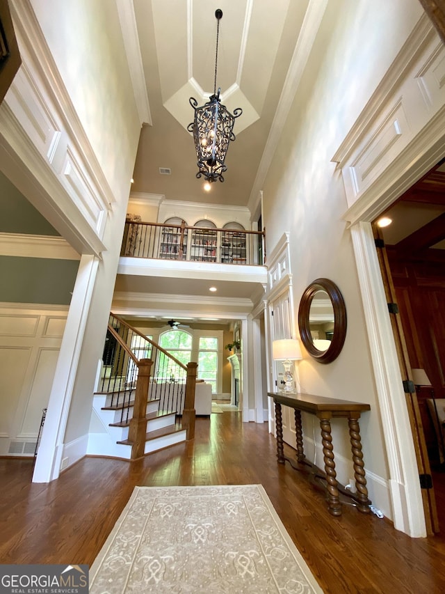 entryway featuring wood finished floors, a towering ceiling, ornamental molding, and stairs