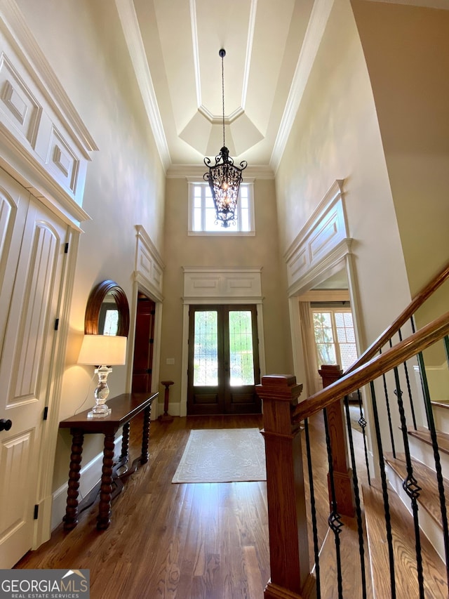 foyer with a tray ceiling, french doors, an inviting chandelier, a towering ceiling, and wood finished floors