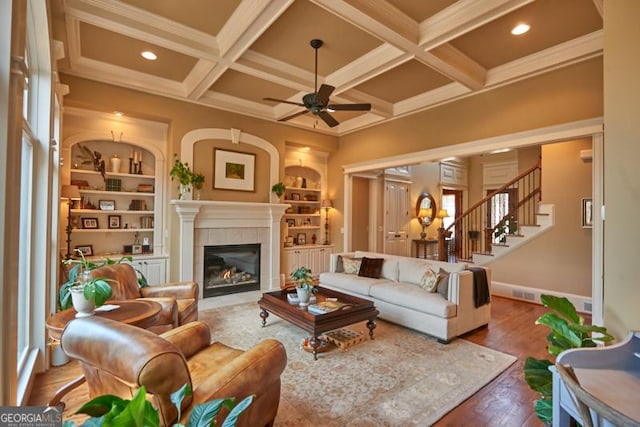 living room featuring coffered ceiling, a tiled fireplace, ceiling fan, wood finished floors, and beam ceiling