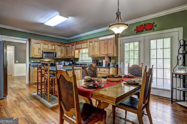 dining space with wainscoting, ornamental molding, light wood-type flooring, and visible vents