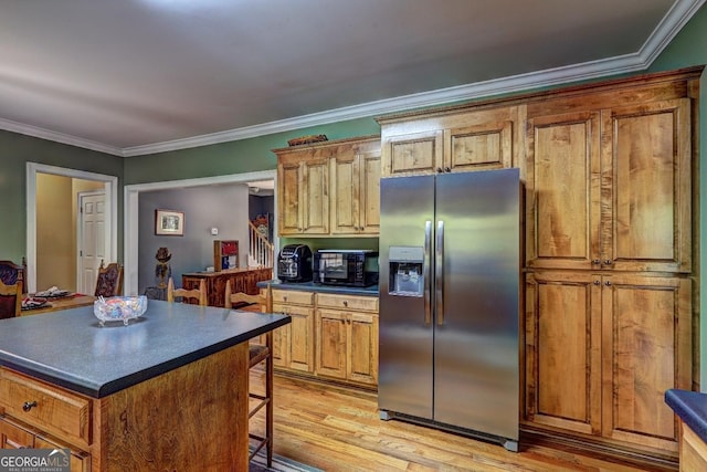 kitchen featuring a kitchen bar, dark countertops, stainless steel refrigerator with ice dispenser, light wood-style floors, and ornamental molding