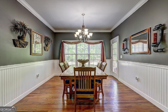 dining space featuring crown molding, a notable chandelier, a wainscoted wall, and wood finished floors