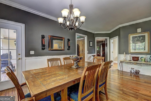 dining area with an inviting chandelier, crown molding, a wainscoted wall, and wood finished floors