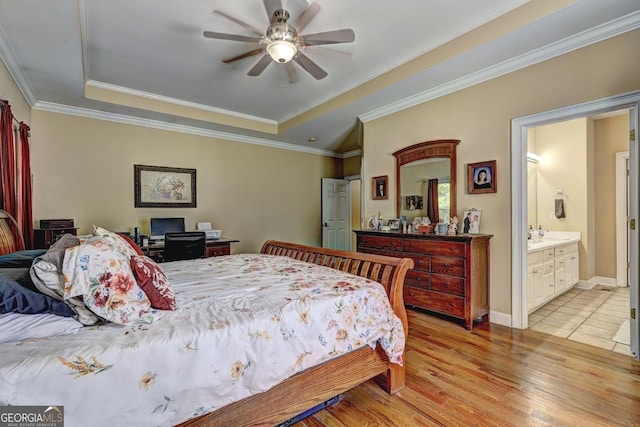 bedroom featuring a tray ceiling, crown molding, ceiling fan, ensuite bath, and light wood-style floors