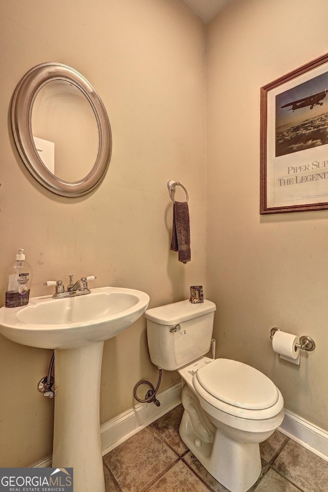 half bath with toilet, baseboards, tile patterned floors, and a sink