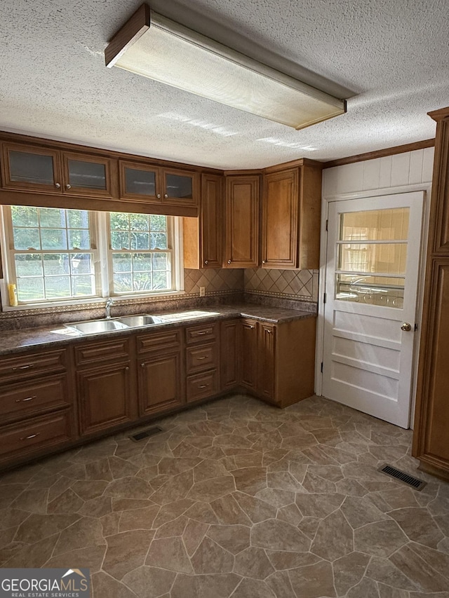 kitchen featuring a textured ceiling, decorative backsplash, dark countertops, and stone flooring