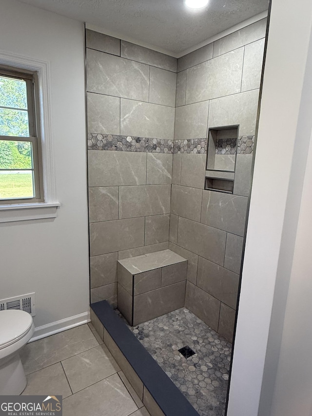 bathroom featuring toilet, a tile shower, tile patterned floors, visible vents, and baseboards
