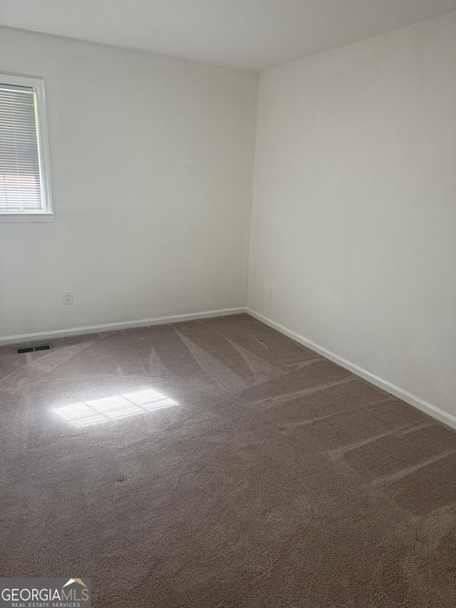 unfurnished room featuring visible vents, baseboards, and dark carpet