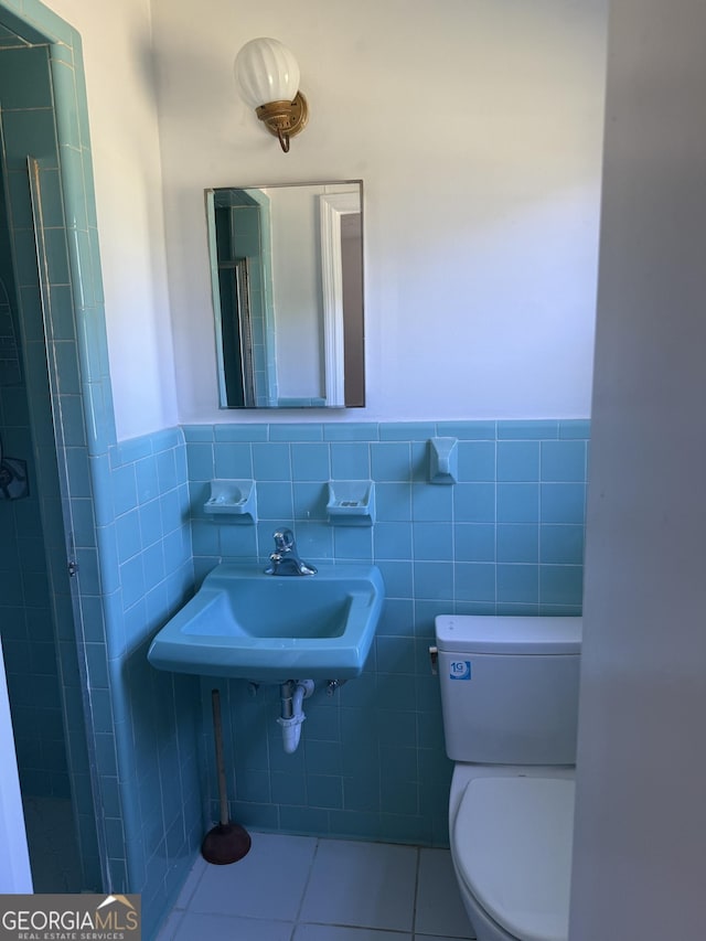 bathroom featuring a sink, tile walls, toilet, a wainscoted wall, and tile patterned floors