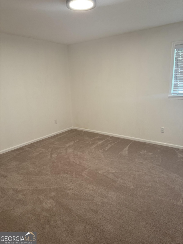 unfurnished room with baseboards and dark carpet