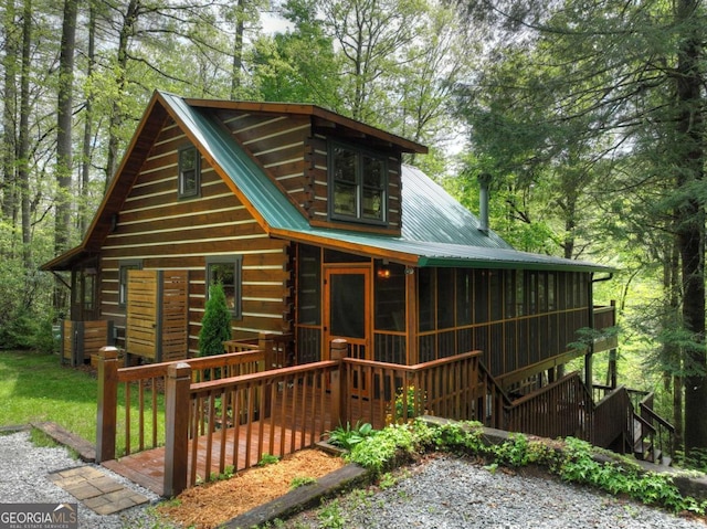 view of front of property with metal roof, a sunroom, log exterior, and a deck