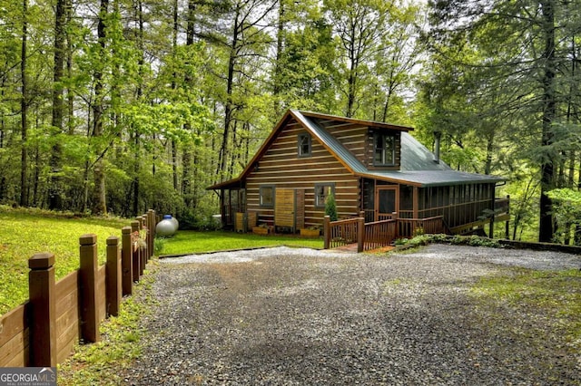 view of front of house with a front yard, a view of trees, driveway, and a wooden deck