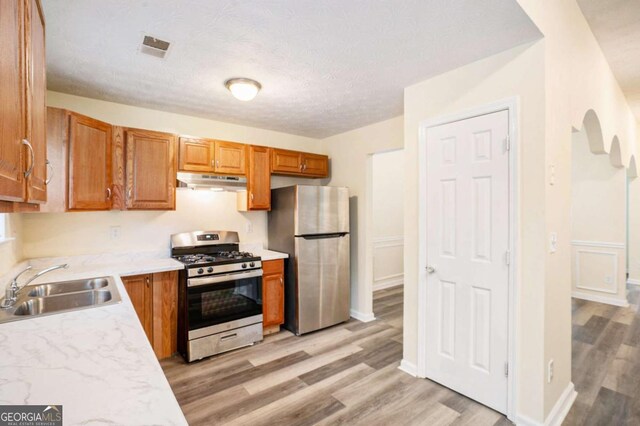 2722 S Hills, Riverdale, GA 30296 - kitchen with under cabinet range hood, light wood finished floors, a sink, brown cabinets, and stainless steel appliances