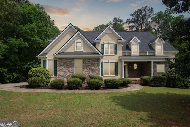 view of front of home with stucco siding, stone siding, and a lawn