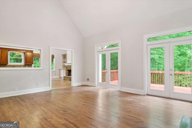 unfurnished living room featuring high vaulted ceiling, hardwood / wood-style flooring, baseboards, and french doors