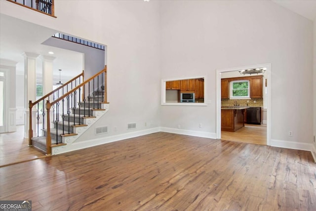 unfurnished living room featuring stairway, visible vents, a towering ceiling, and hardwood / wood-style flooring