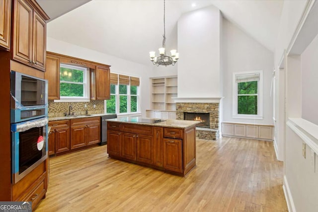 kitchen with brown cabinetry, an inviting chandelier, light wood-style flooring, a stone fireplace, and appliances with stainless steel finishes