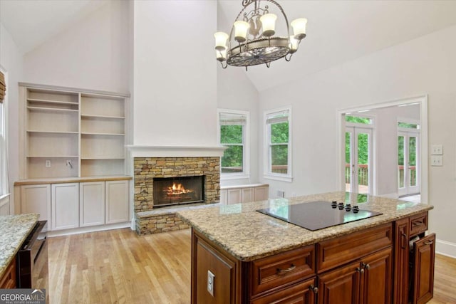 kitchen with a chandelier, black electric cooktop, light stone countertops, a kitchen island, and light wood-style floors