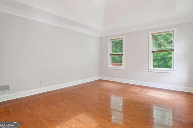 empty room with crown molding, visible vents, wood finished floors, and baseboards
