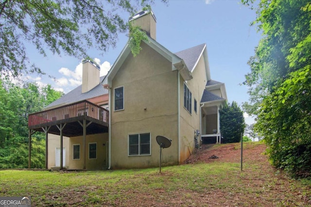 rear view of house featuring a chimney, a deck, stucco siding, and a yard