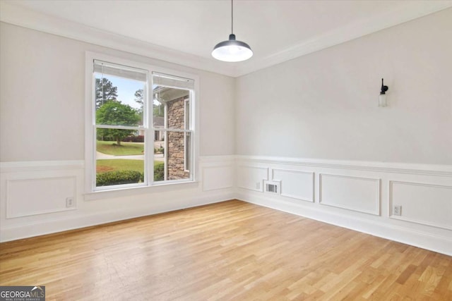 unfurnished dining area with a decorative wall, visible vents, light wood-style flooring, and wainscoting