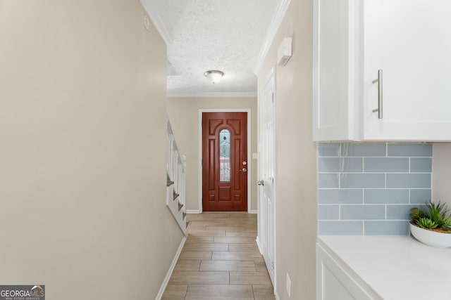 entryway with a textured ceiling, light wood-type flooring, crown molding, and baseboards