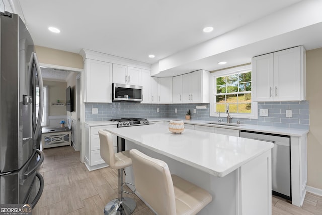 kitchen featuring appliances with stainless steel finishes, a sink, light countertops, a breakfast bar, and recessed lighting