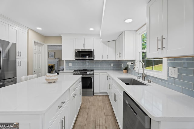 kitchen featuring appliances with stainless steel finishes, a sink, a center island, decorative backsplash, and white cabinetry