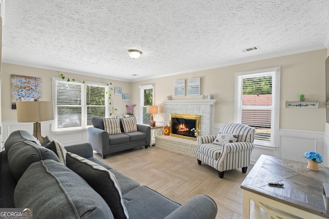 living room featuring crown molding, wainscoting, a fireplace, and a textured ceiling