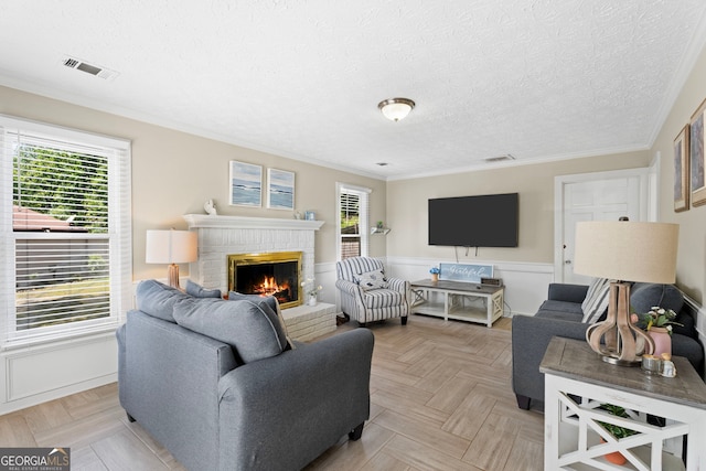 living area featuring a fireplace, crown molding, healthy amount of natural light, a wainscoted wall, and a textured ceiling