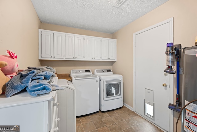 clothes washing area with washing machine and clothes dryer, water heater, cabinet space, and a textured ceiling