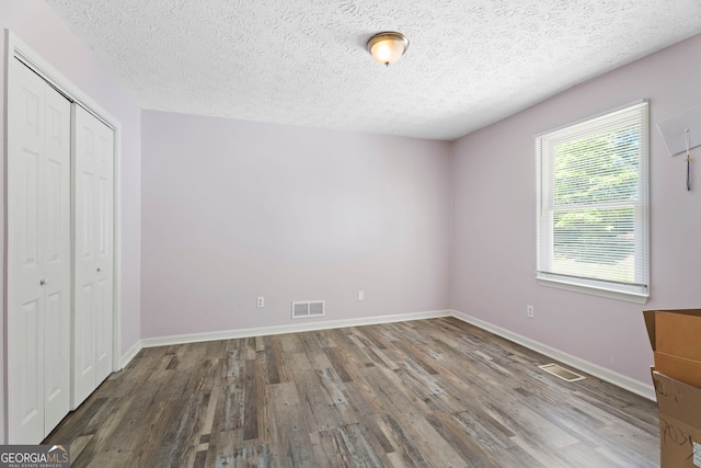 unfurnished bedroom with wood finished floors, a closet, a textured ceiling, and baseboards