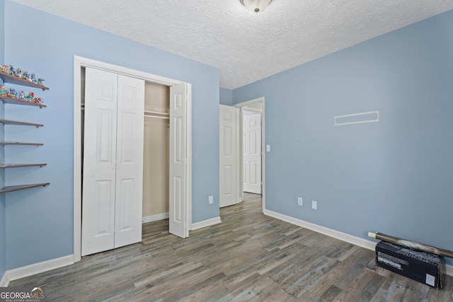 unfurnished bedroom featuring wood finished floors, baseboards, a closet, and a textured ceiling
