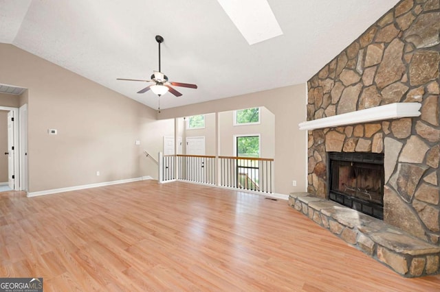 unfurnished living room with a ceiling fan, lofted ceiling with skylight, visible vents, wood finished floors, and a fireplace