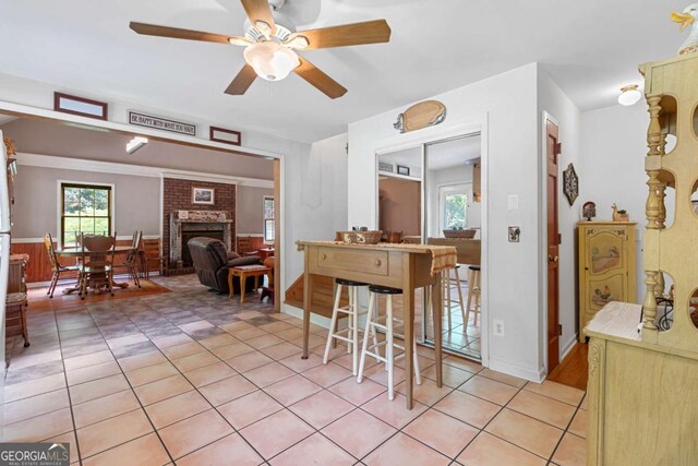 dining space with ceiling fan, plenty of natural light, a fireplace, and light tile patterned floors