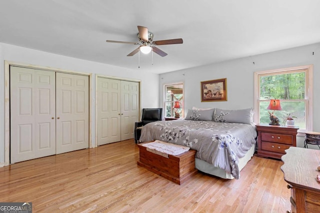 bedroom with light wood finished floors, two closets, and a ceiling fan